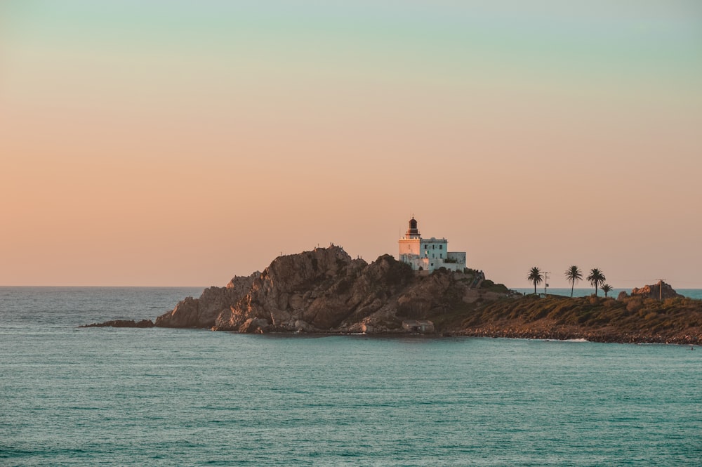 Faro blanco y marrón en la parte superior de la formación rocosa marrón cerca del cuerpo de agua durante el día