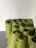 A collection of rolled-up green yoga mats are stacked against a plain white wall. The mats are tightly wound and arranged neatly on a gray floor, forming a cluster.