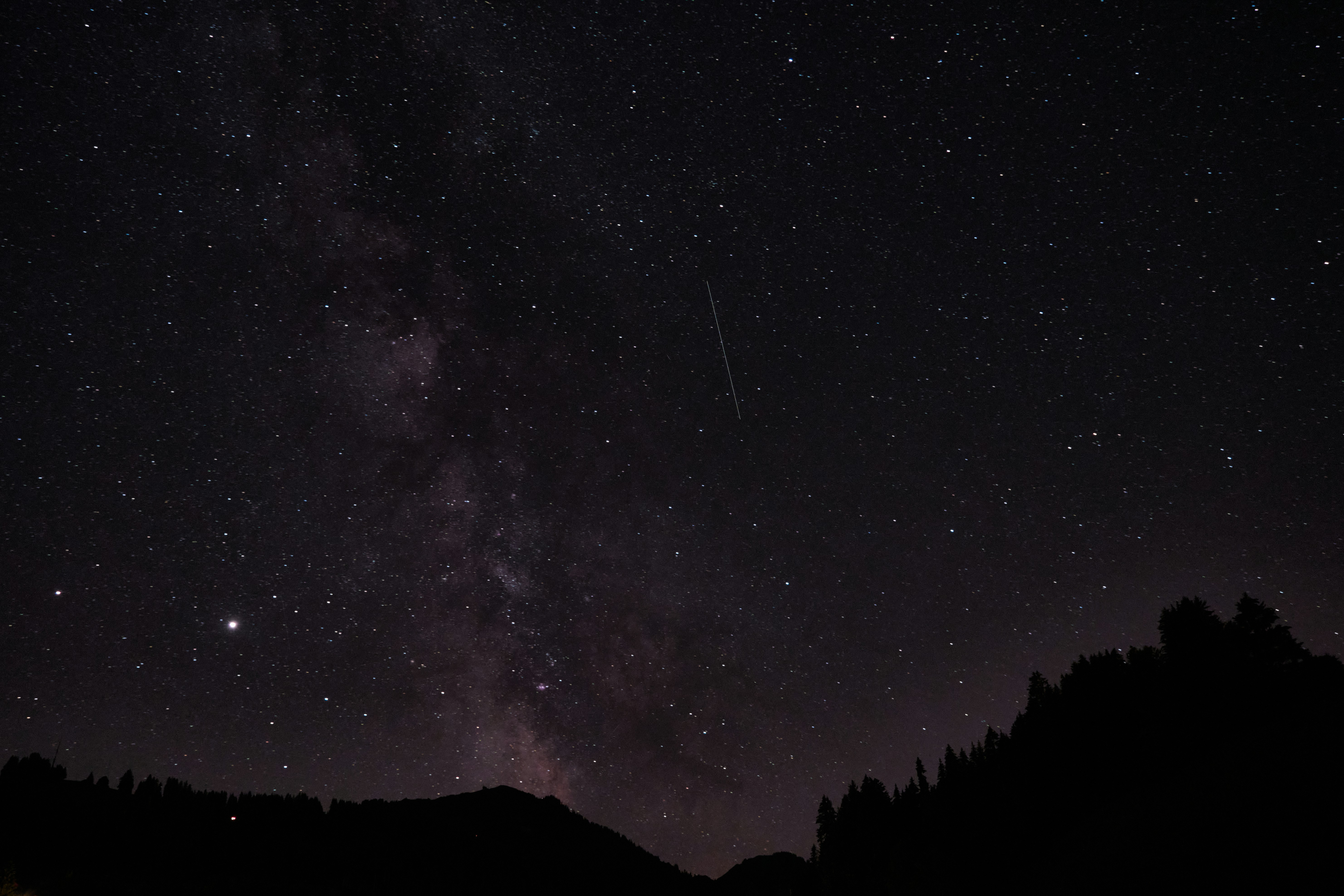 Céu noturno com constelações visíveis sobre montanhas silhuetadas, atmosfera contemplativa e estrelada