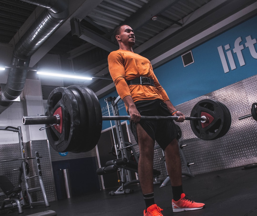 man in orange crew neck t-shirt carrying black barbell