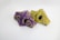 Two intricately designed face masks are laying side by side. One mask features a vibrant purple background with yellow and black paisley patterns, while the other displays a bright yellow backdrop with similar designs in purple and black. Both masks have black filters on the sides.