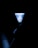 A shuttlecock is illuminated with a bright light against a dark background, while a hand is faintly visible holding it at the bottom. The object's intricate pattern contrasts sharply with the surrounding darkness.
