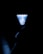 A shuttlecock is illuminated with a bright light against a dark background, while a hand is faintly visible holding it at the bottom. The object's intricate pattern contrasts sharply with the surrounding darkness.