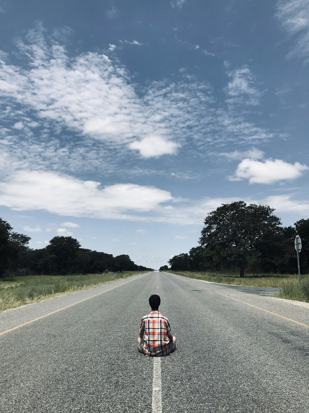 Persona con camisa a cuadros roja y negra caminando por una carretera de asfalto gris durante el día