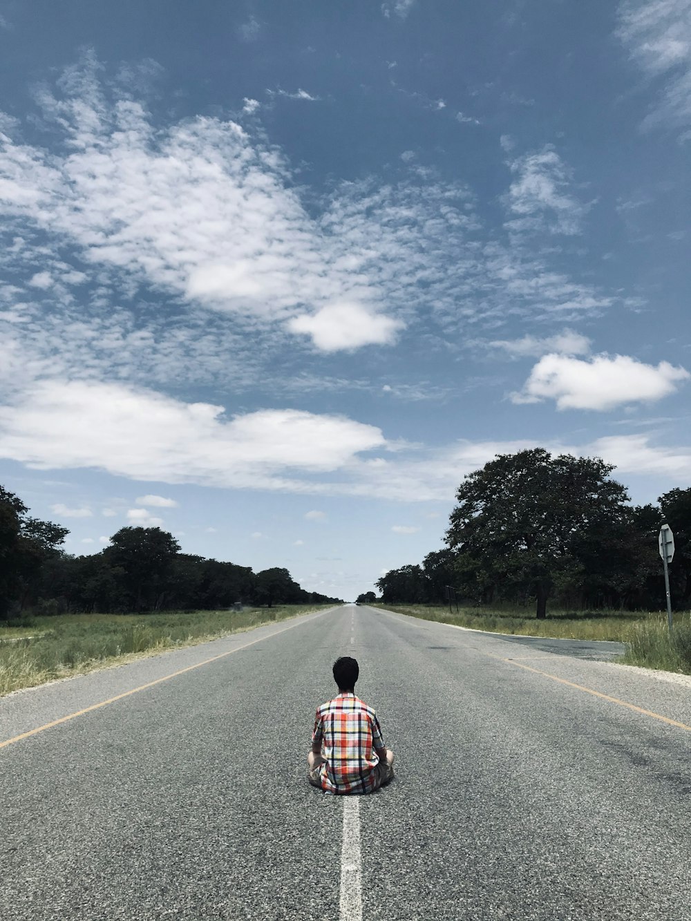 person in red and black plaid shirt walking on gray asphalt road during daytime