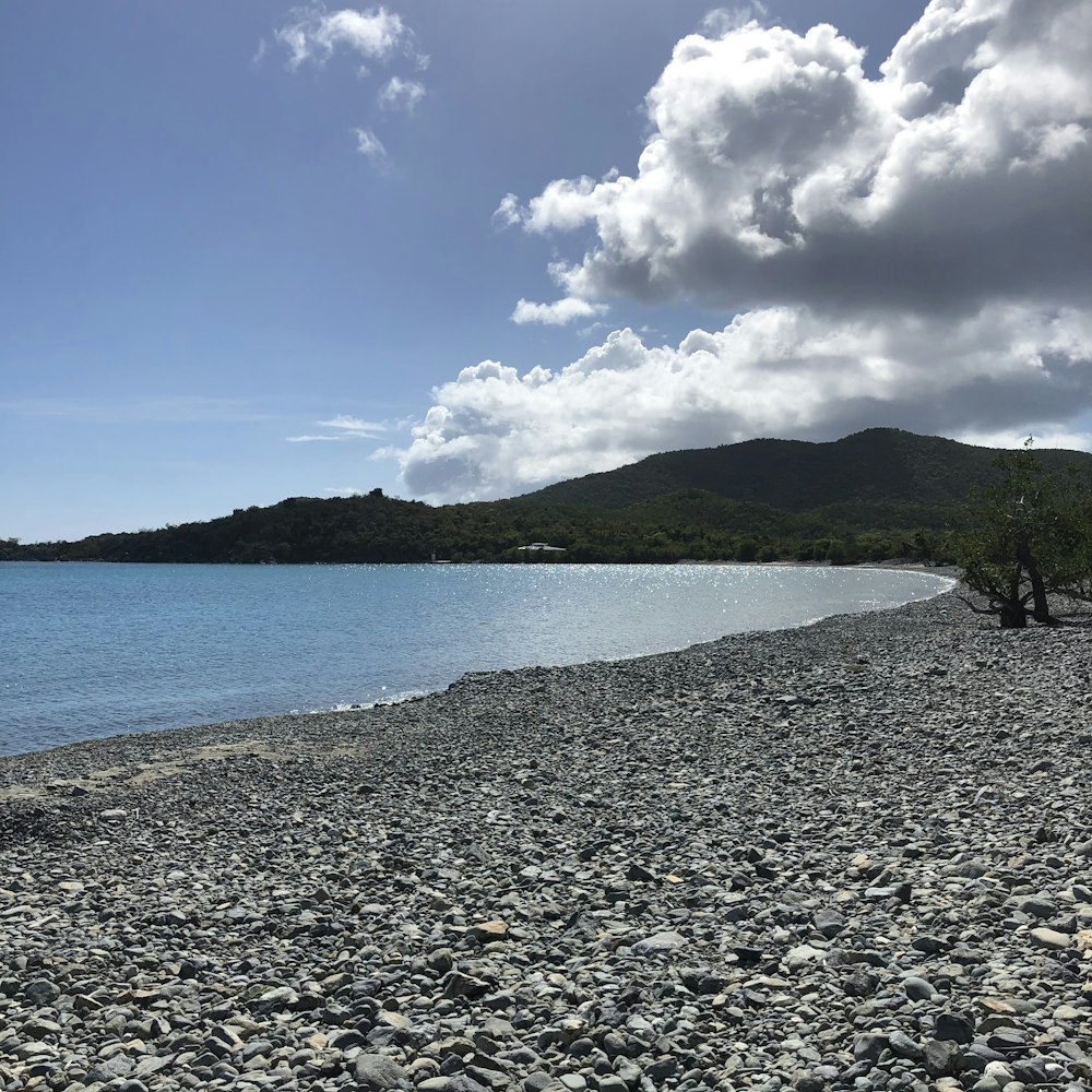 body of water near green mountain under blue and white sunny cloudy sky during daytime