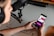 A person wearing headphones is seated at a desk with a microphone setup and a keyboard. They are holding a smartphone displaying a colorful audio recording app interface, with options for starting and managing recordings.