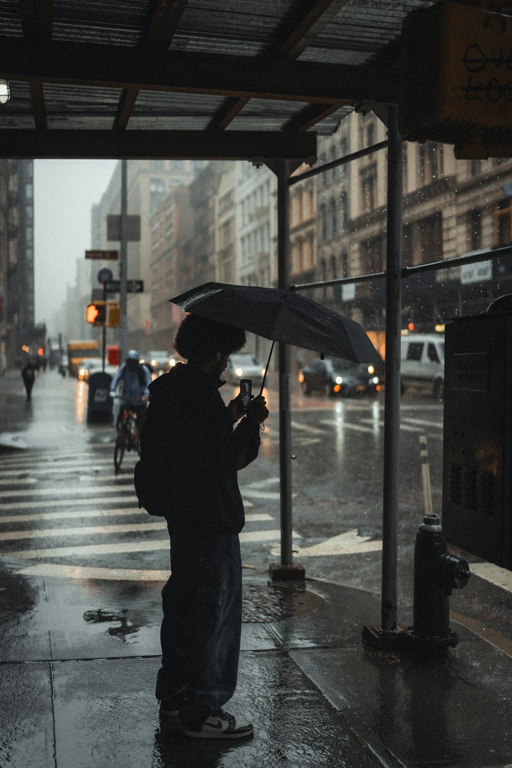 man in black jacket holding umbrella standing on sidewalk during daytime