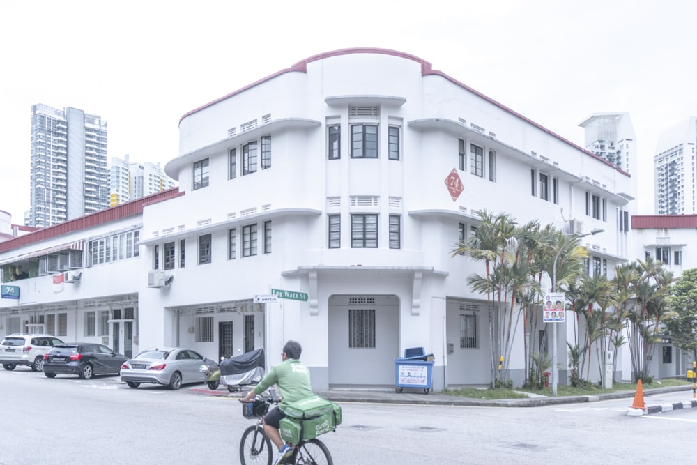 man in green shirt riding bicycle near white concrete building during daytime