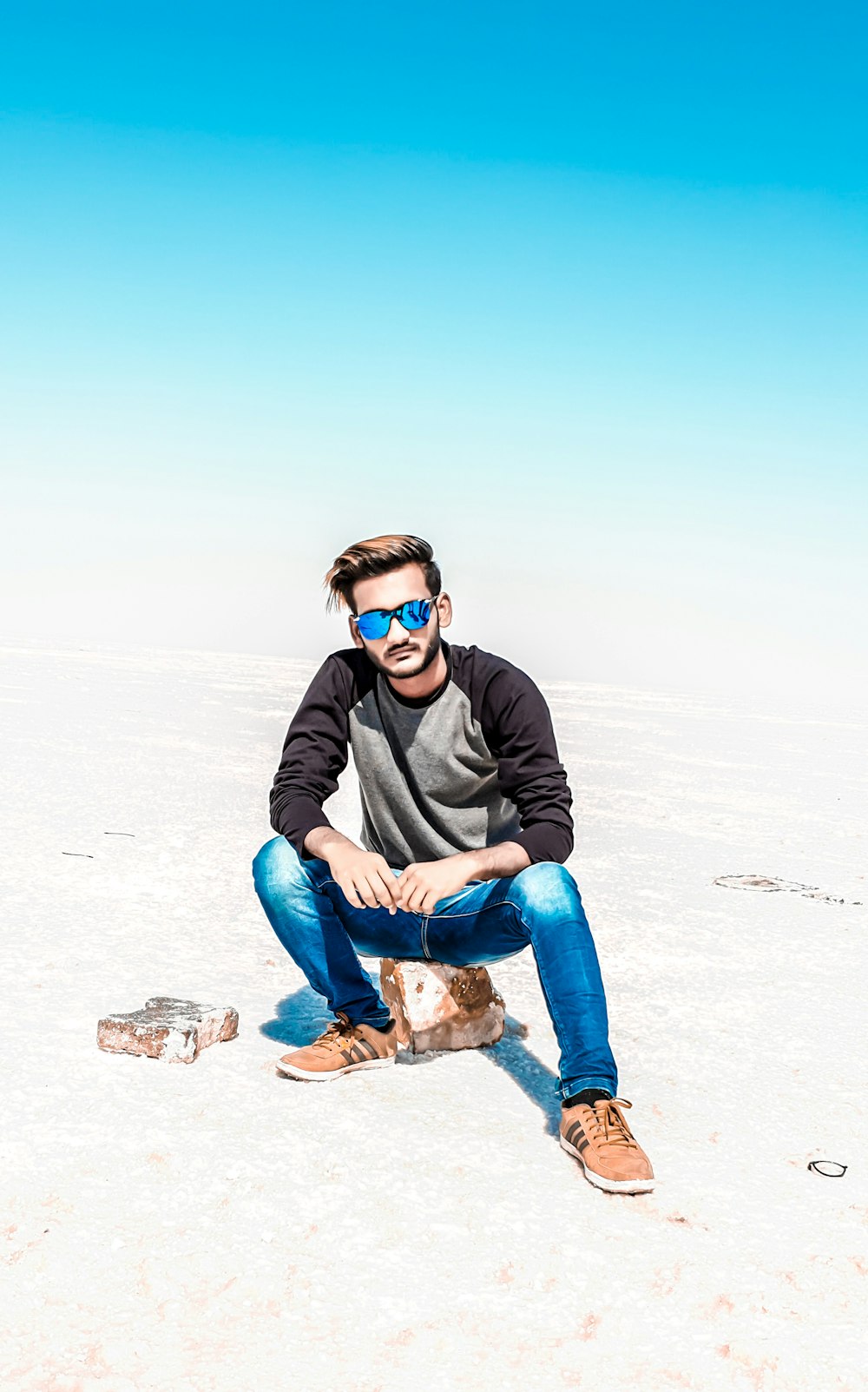 man in black jacket and blue denim jeans sitting on rock during daytime