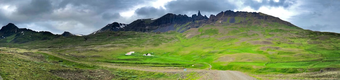 green grass field near mountain under white clouds during daytime