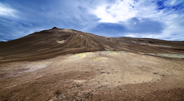 Experienced prospector examining soil samples near a wide natural valley under clear skies.