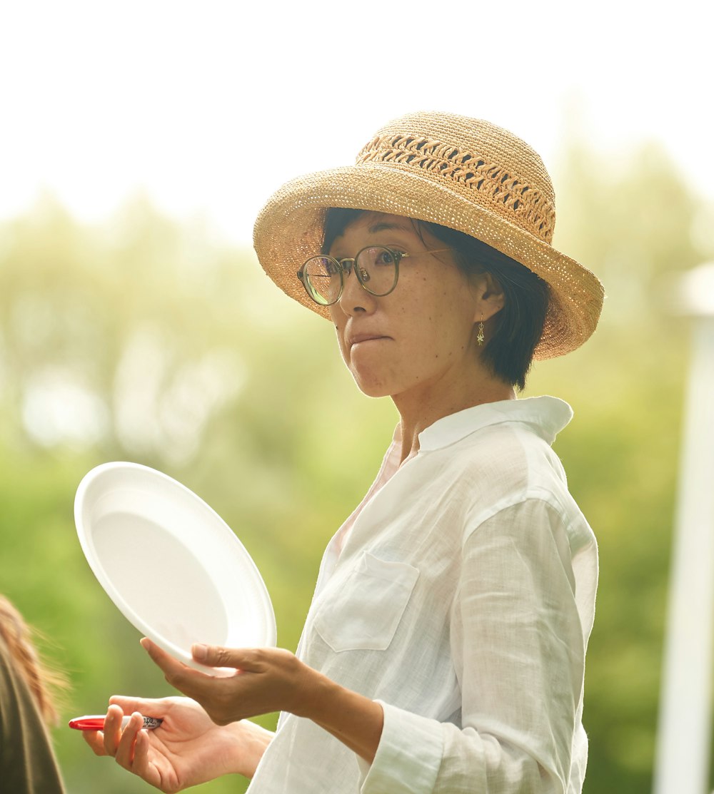 woman in white dress shirt wearing brown hat holding white round plate during daytime