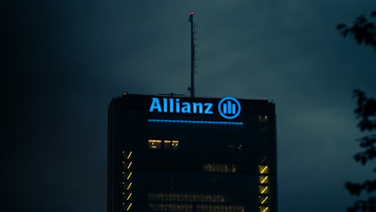The top of a high-rise building is illuminated with blue light, showcasing the Allianz logo prominently. The surrounding sky is dark, creating a stark contrast with the building's lights.