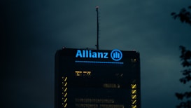 The top of a high-rise building is illuminated with blue light, showcasing the Allianz logo prominently. The surrounding sky is dark, creating a stark contrast with the building's lights.