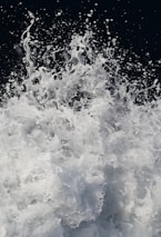 A dynamic and energetic splash of water captured mid-action with droplets and foam suspended in the air against a dark background. The movement creates a sense of power and fluidity.