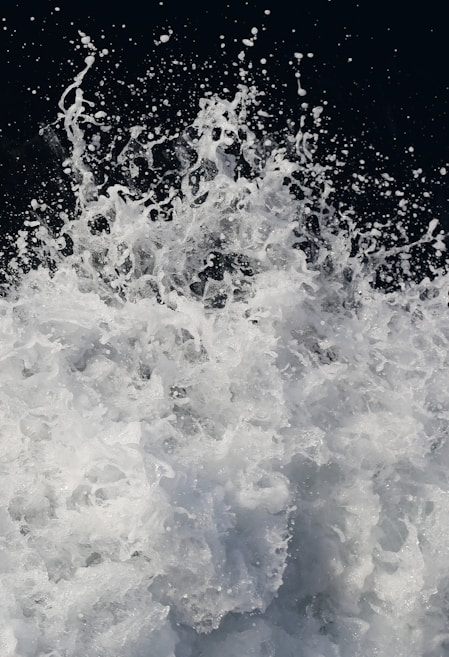 A dynamic and energetic splash of water captured mid-action with droplets and foam suspended in the air against a dark background. The movement creates a sense of power and fluidity.