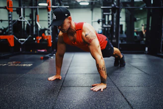 man in red tank top and black shorts doing push up on the street