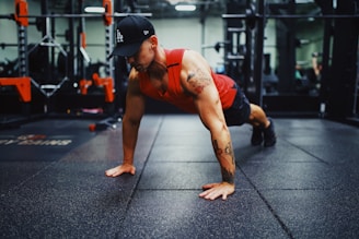 man in red tank top and black shorts doing push up on the street