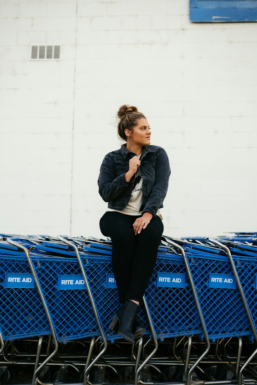 Mujer en chaqueta gris y pantalones negros de pie junto al carrito de compras azul