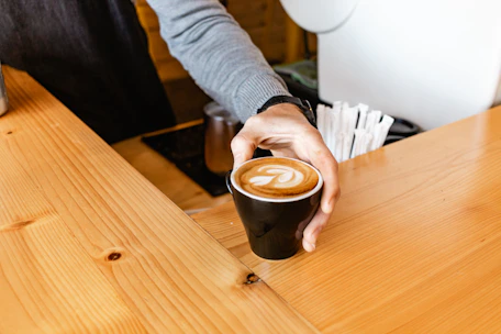 A friendly barista handing over a warm cup of coffee with latte art to a smiling customer.