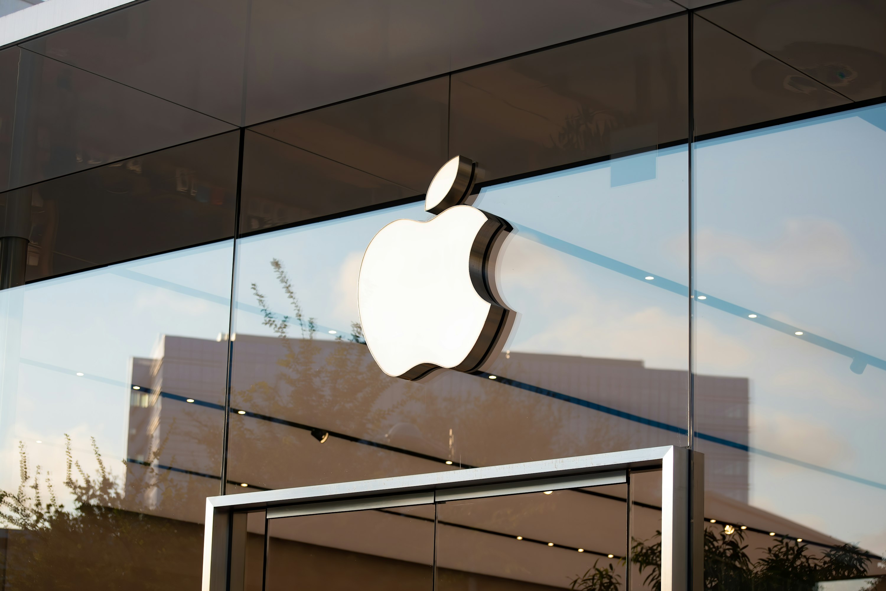 Maçã trincada da Apple num vidro que integra a fachada de um edifício. Abaixo, vê-se a parte superior de uma porta de vidro.