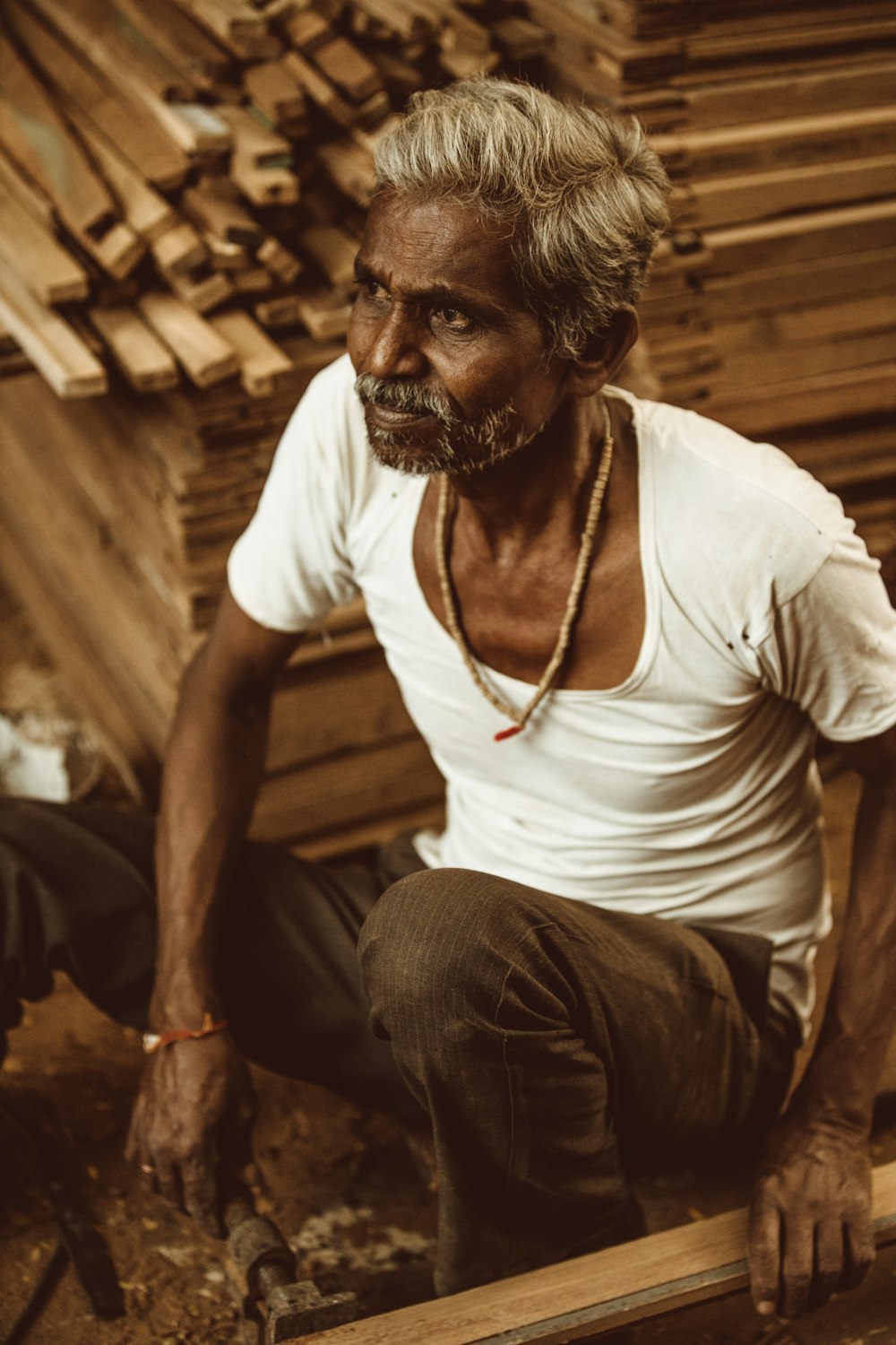 man in white crew neck t-shirt and brown pants sitting on brown wooden chair