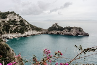 body of water near mountain under white clouds during daytime