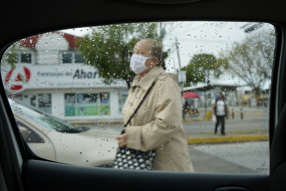 woman in beige coat standing on sidewalk during daytime