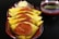 A serving dish contains several yellow chapatis folded over slices of spicy sausage, topped with garnish such as carrots and an onion flower. A small bowl of green chutney is placed beside the dish.