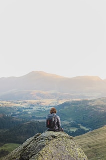 A traveler pausing on a rocky cliff, gazing out over a vast, colorful valley.