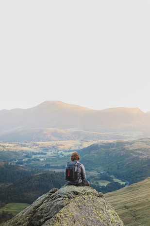 A traveler pausing on a rocky cliff, gazing out over a vast, colorful valley.