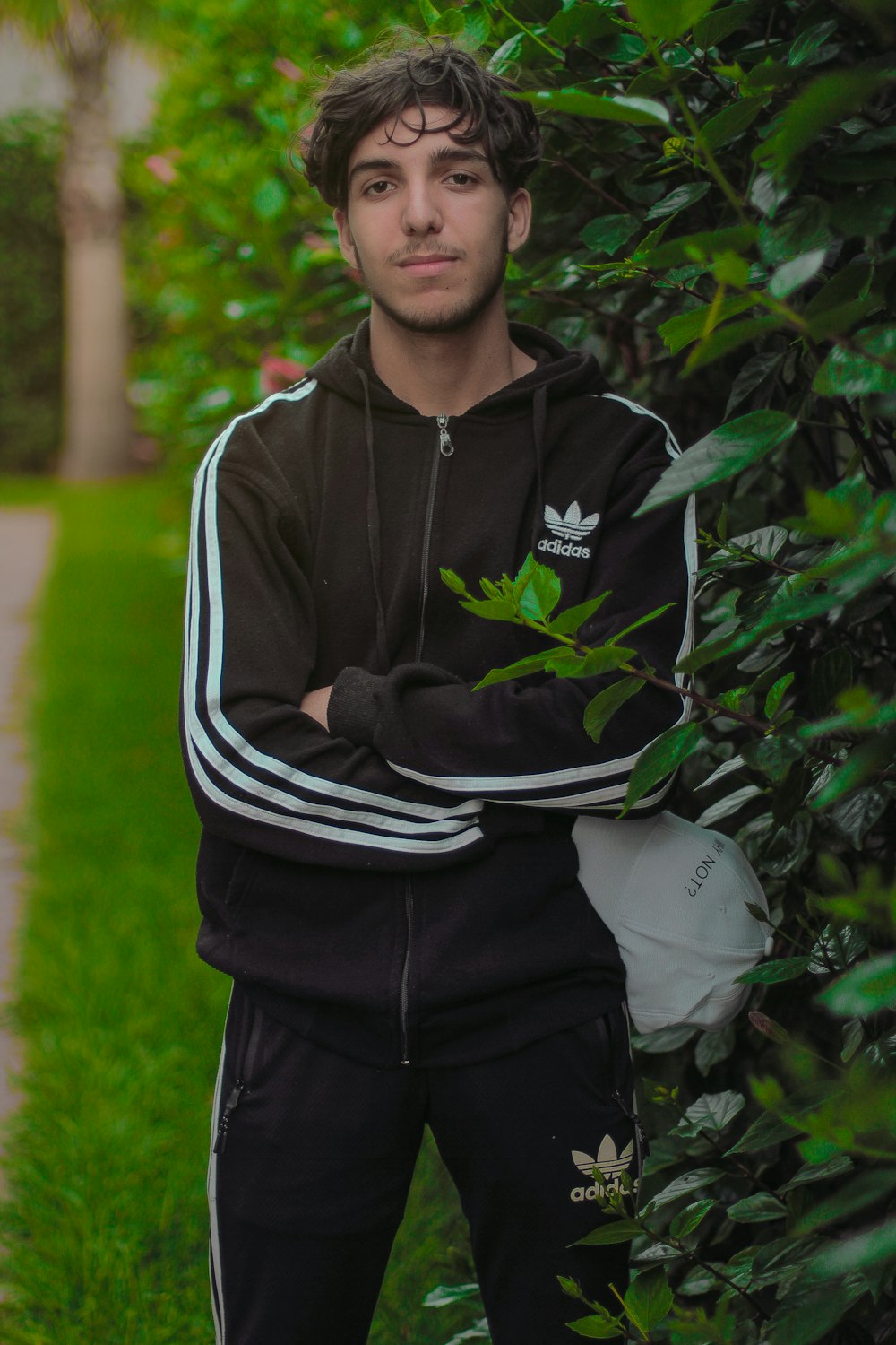 man in black and white zip up jacket standing beside green plant during daytime