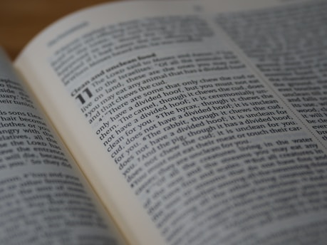 An open book displays text in clear print, with a passage highlighted by larger bold numbers, suggesting a chapter or section start. The text is printed in two columns on slightly yellowed pages, indicating age or frequent use.