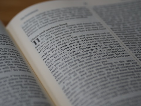 An open book displays text in clear print, with a passage highlighted by larger bold numbers, suggesting a chapter or section start. The text is printed in two columns on slightly yellowed pages, indicating age or frequent use.