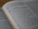 An open book displays text in clear print, with a passage highlighted by larger bold numbers, suggesting a chapter or section start. The text is printed in two columns on slightly yellowed pages, indicating age or frequent use.