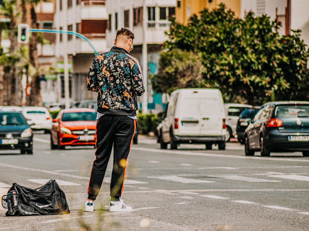 Homme en chemise à manches longues à fleurs noires et blanches et pantalon marron tenant un sac en cuir noir