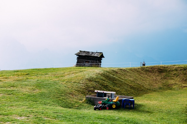 A cozy family moment on a small farm with children playing near garden beds and a rustic farmhouse in the background.