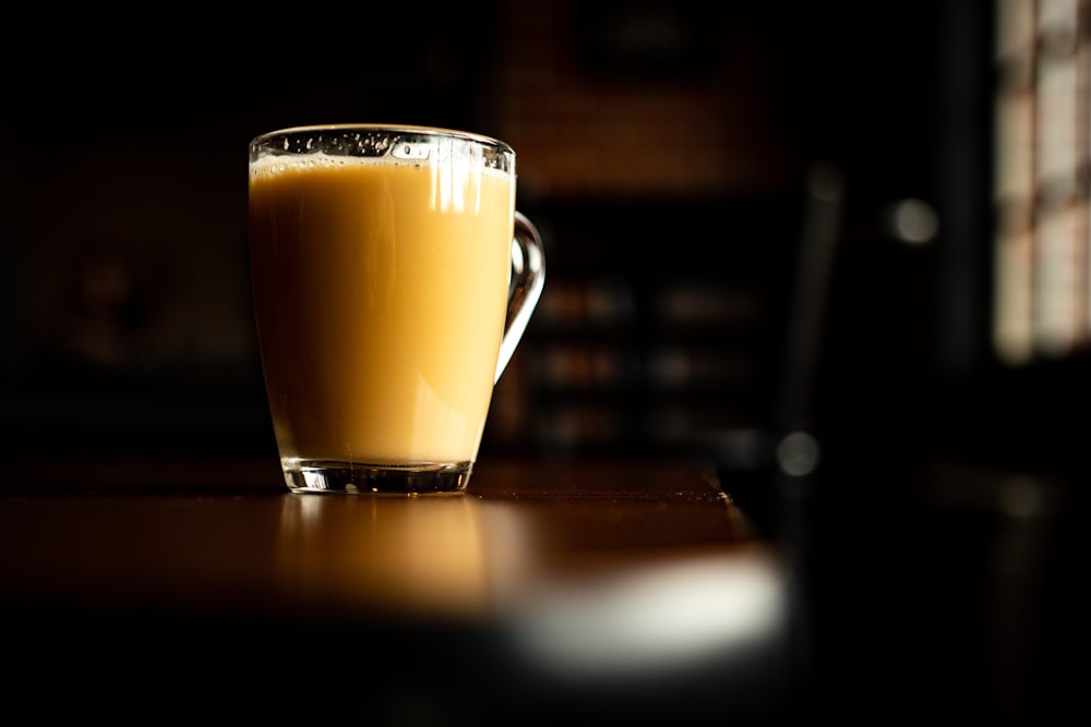 clear glass mug with brown liquid on brown wooden table