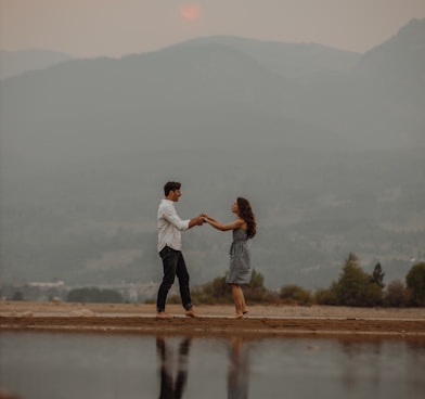 man and woman kissing on brown field near lake during daytime