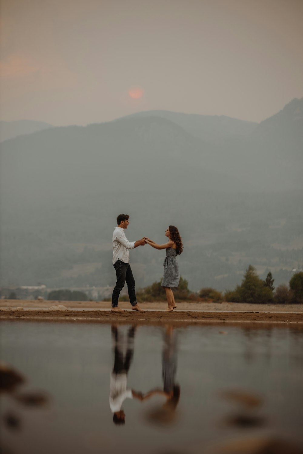 man and woman kissing on brown field near lake during daytime