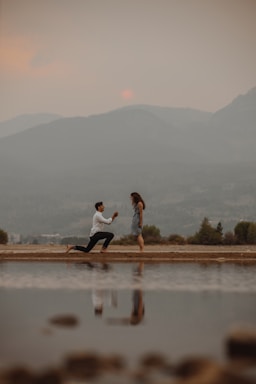 the knee,how to photograph man in white shirt and black pants sitting on brown wooden dock during daytime