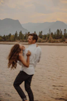 A couple playfully splashing water at each other near a lake.