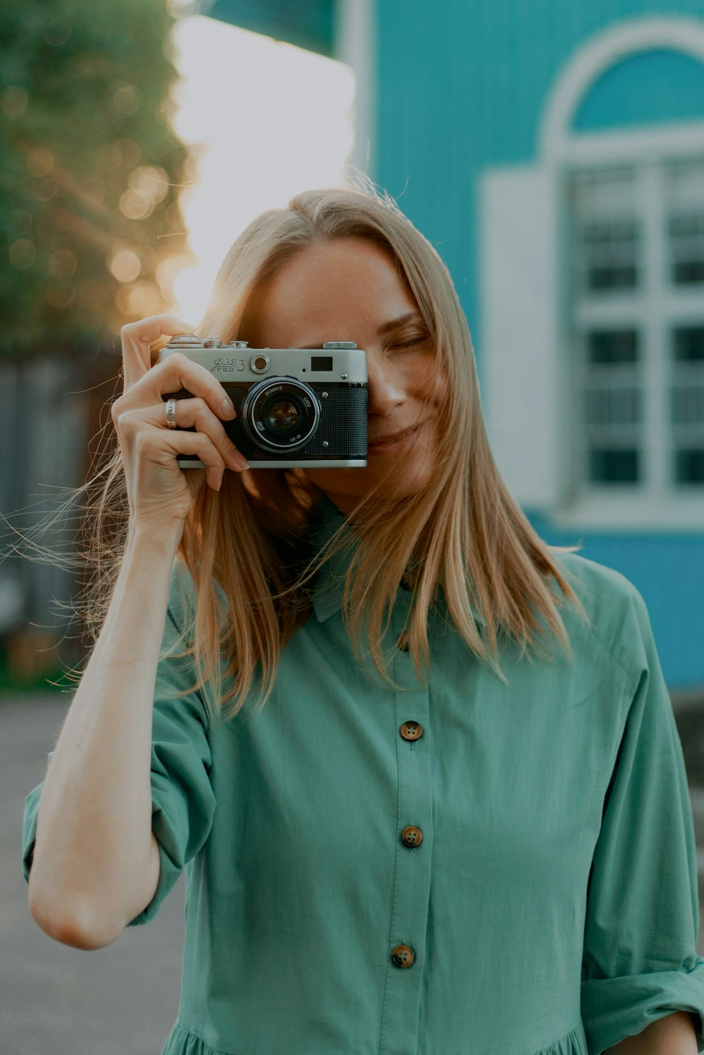 Mujer con camisa verde azulado con botones sosteniendo una cámara plateada