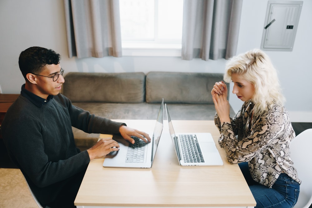 a man and woman sitting at a table with laptops