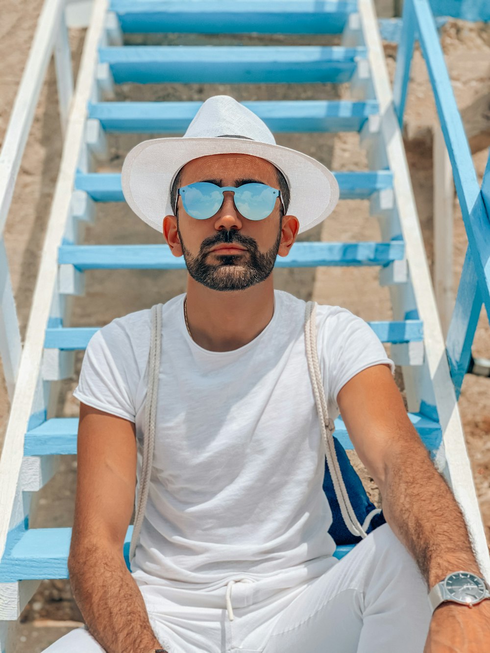 Mann im weißen Rundhals-T-Shirt mit Sonnenbrille sitzt auf weißem Holzstuhl