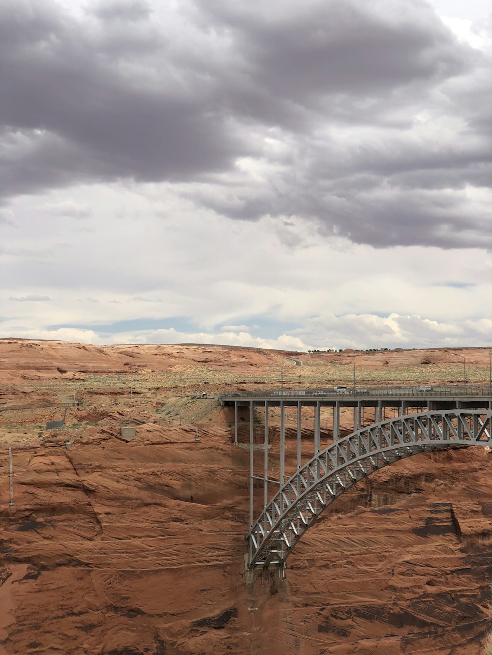 gray metal bridge over brown rock formation under white clouds during daytime