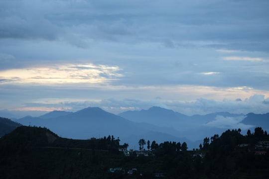 green trees and mountains under white clouds during daytime in Pauri India
