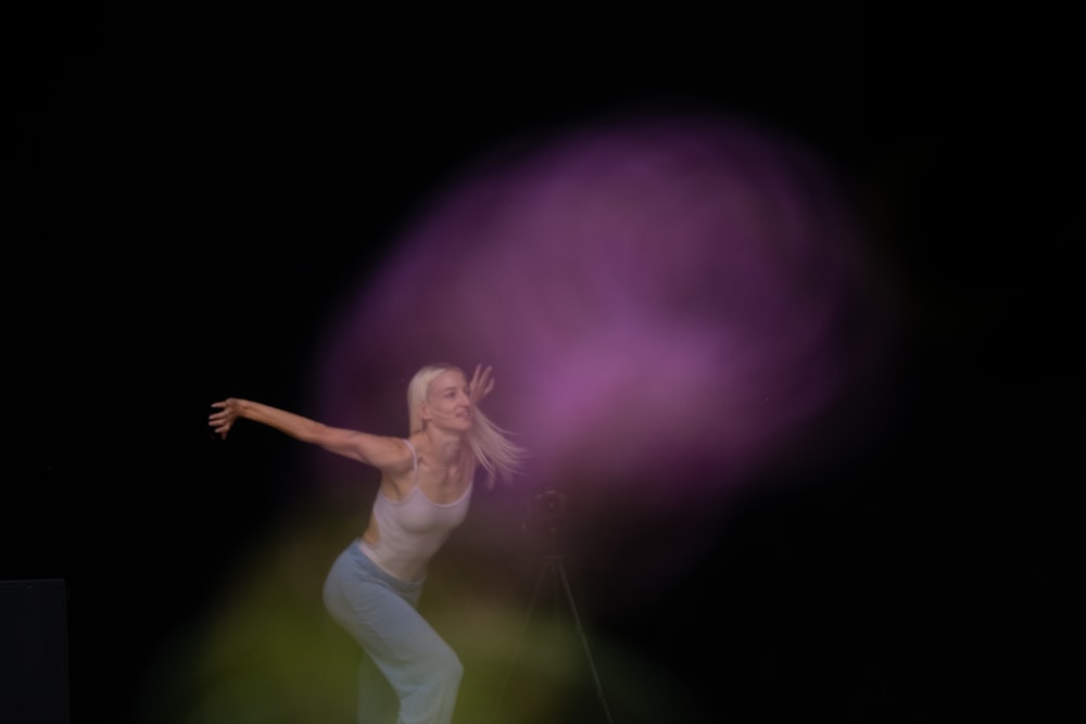 Mujer con camiseta blanca sin mangas y pantalones blancos saltando sobre luz púrpura