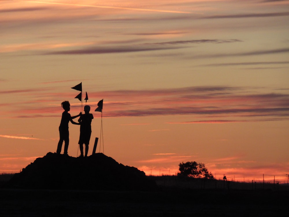 silhouette of 2 person standing on rock during sunset